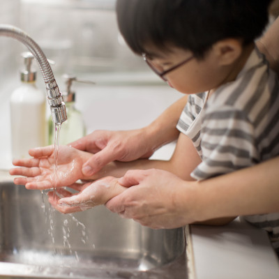 A young child washes their hands, helped by a parent out-of-frame